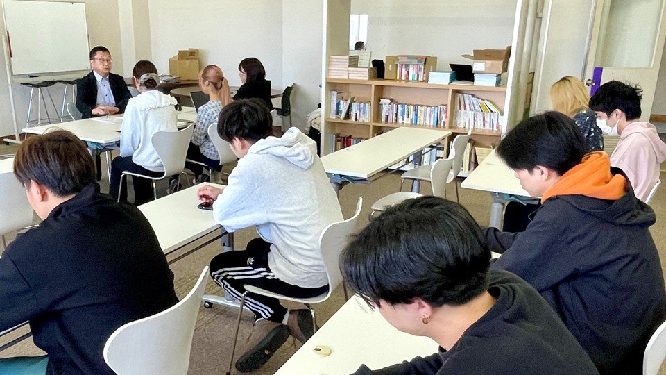 新聞記者の取材を学生たちが見学している